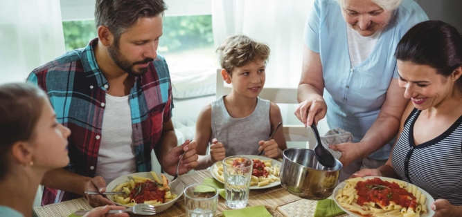 Die Großfamilie isst an einem Tisch Penne mit Tomatensauce.