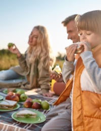 Paar mit zwei Kindern beim Picknick in der Sonne.