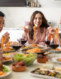 Fünf junge Menschen essen gemeinsam Spaghetti mit Tomatensoße an einem großen Tisch.