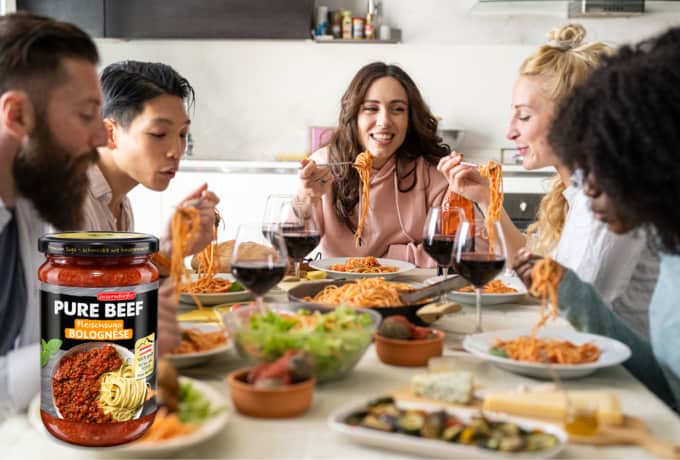 Fünf junge Menschen essen gemeinsam Spaghetti mit Tomatensoße an einem großen Tisch und Sugo Bolognese.