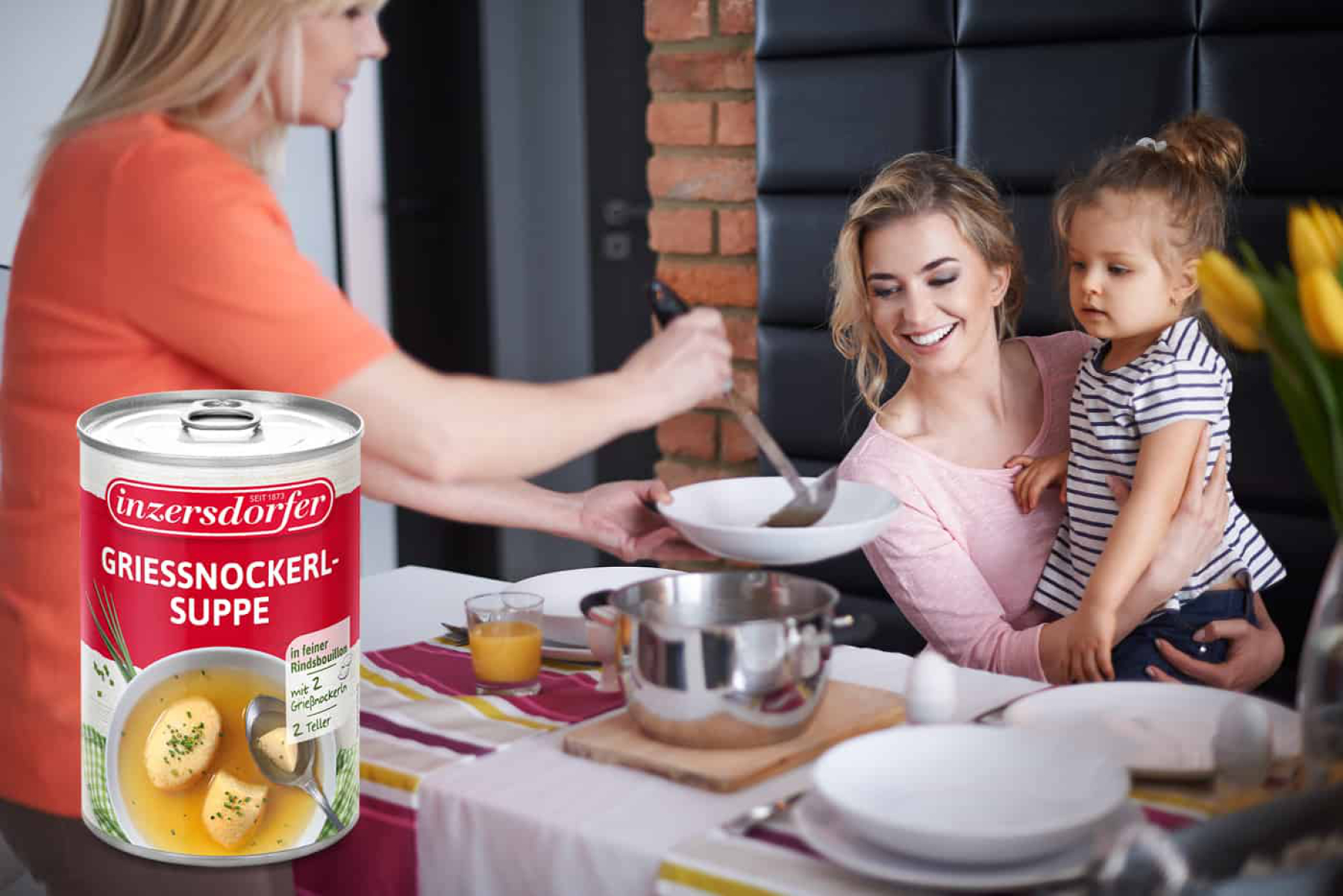 Ältere Frau serviert einer jungen Frau mit Kind auf dem Arm, Essen auf einem Suppenteller und Grießnockerlsuppe.