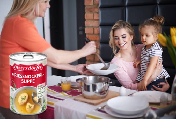 Ältere Frau serviert einer jungen Frau mit Kind auf dem Arm, Essen auf einem Suppenteller und Grießnockerlsuppe.