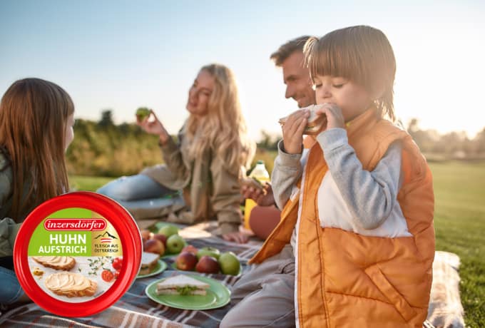 Paar mit zwei Kindern beim Picknick in der Sonne und Huhnaufstrich.
