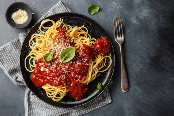 Teller mit Spaghetti und Bolognese-Sugo, garniert mit Basilikum und Parmesan.