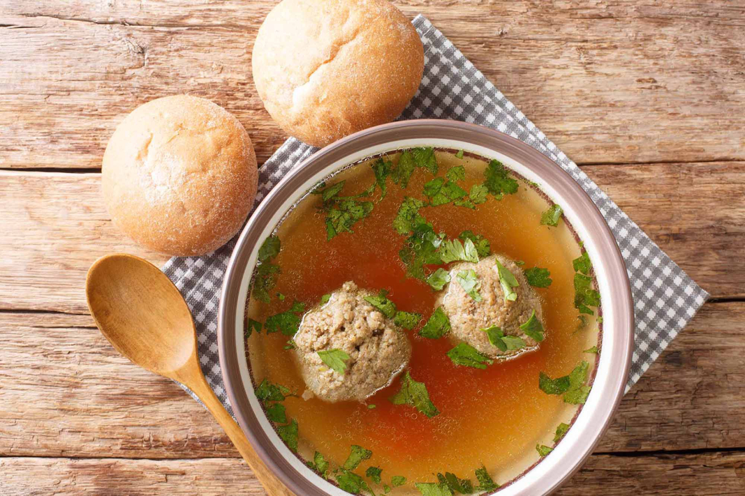 Leberknödelsuppe in einer Suppenschüssel mit klarer Brühe, Petersilie und frischen Brötchen.