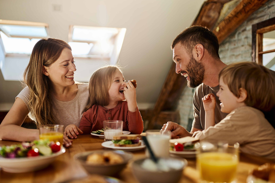 Fröhliche Familie mit Mutter, und Vater und zwei Kindern isst gemeinsam Frühstück an einem Tisch.